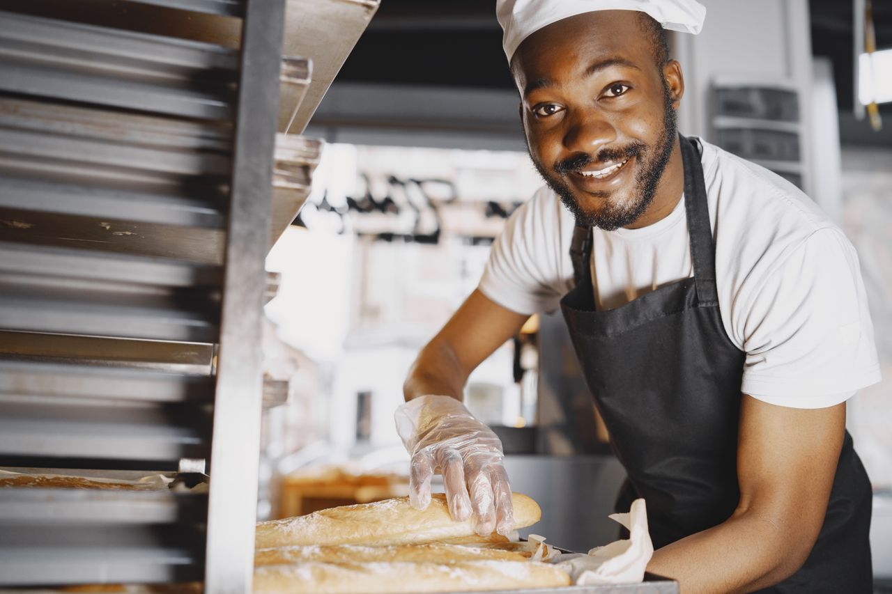 Cheerful male baker showcasing freshly baked baguettes in a bakery setting.