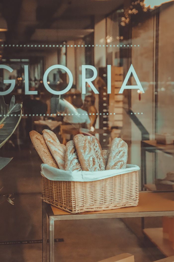 A basket of assorted artisan breads displayed inside a cafe window, evoking a warm, inviting atmosphere.